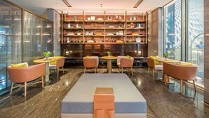 A modern lounge area with a central seating area, bookshelves, and a view of a building.