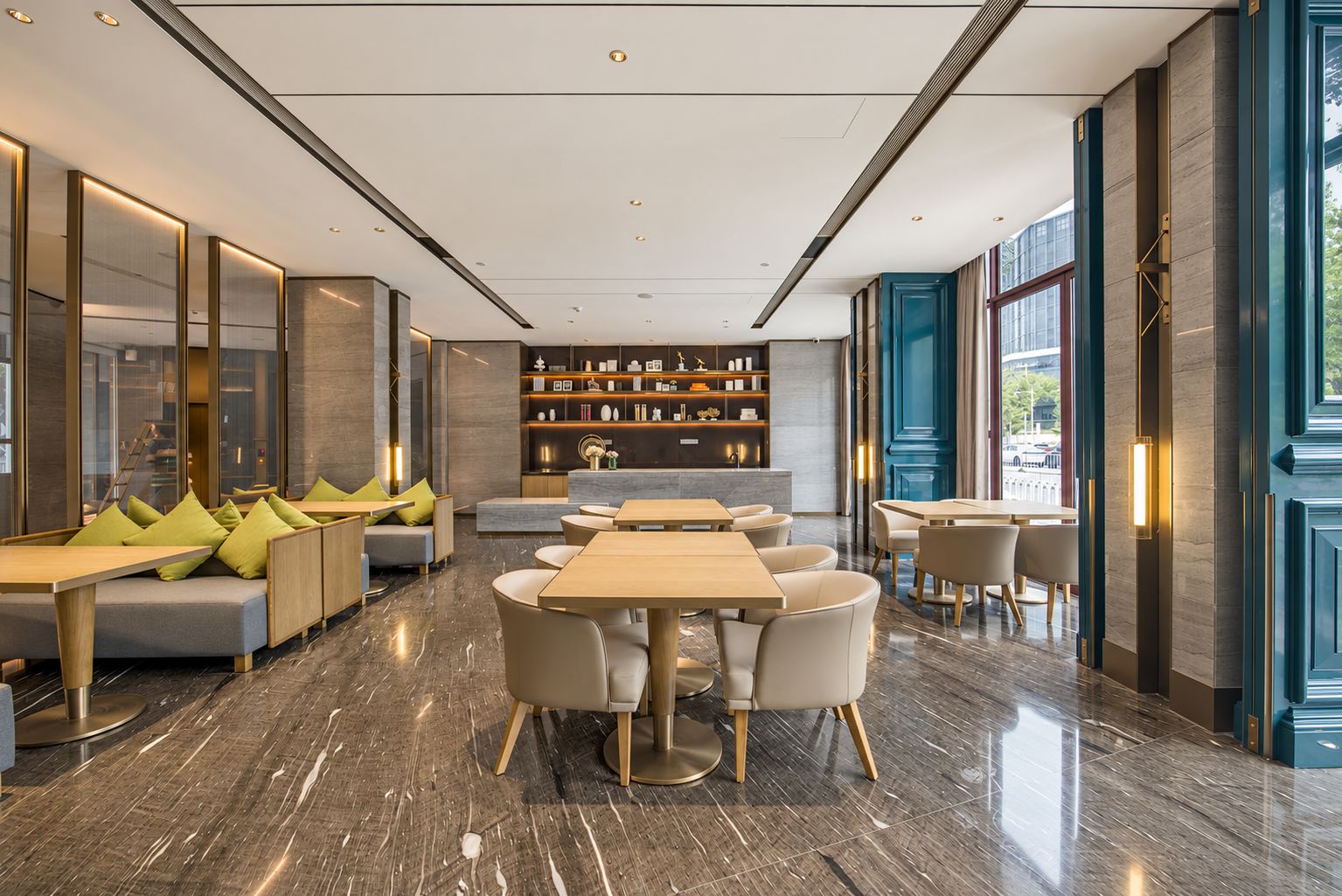 Een moderne hotel lobby met een centraal zitgedeelte, een receptiebalie en uitzicht op de straat.