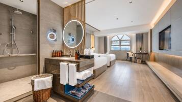 A modern hotel bathroom with a shower, a vanity with a mirror, and a seating area with a table and chairs.