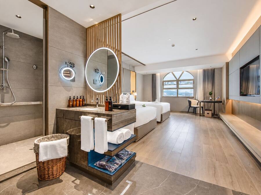 A modern hotel bathroom with a shower, a vanity with a mirror, and a seating area with a table and chairs.