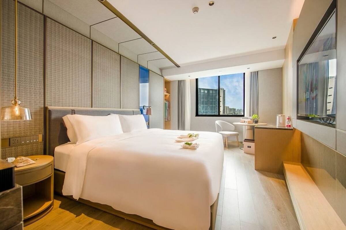 Une chambre d’hôtel moderne, dotée d’un grand lit, d’un bureau, d’une chaise et offrant une vue sur la ville.