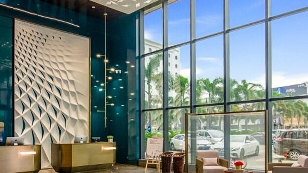 A modern lobby with a geometric wall design, a reception desk, and a large window offering a view of the street.