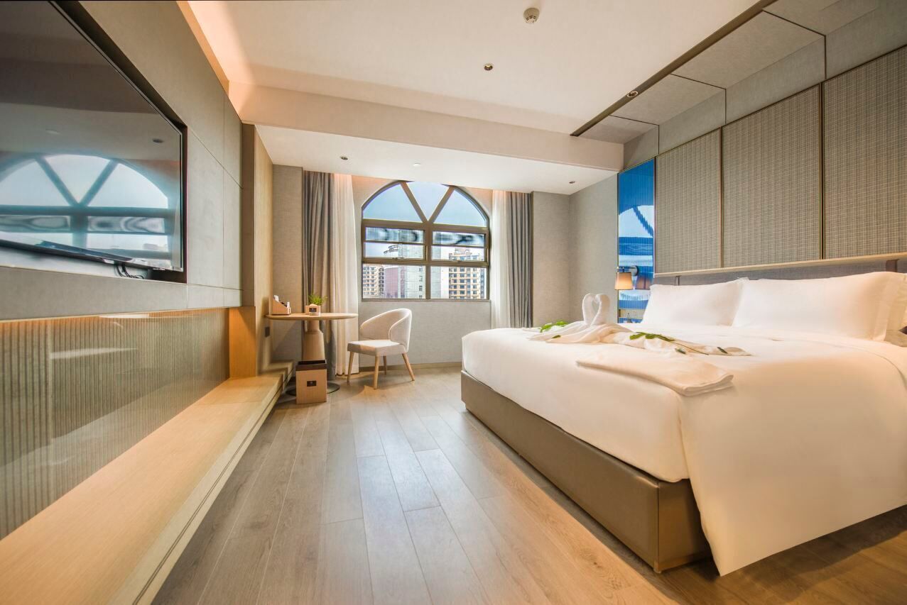 Ein modernes Hotelzimmer mit einem großen Bett, einem Schreibtisch, einem Sessel und einem großen Fenster mit Stadtblick.