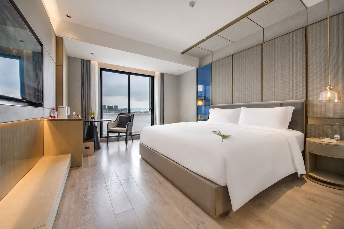 Et moderne hotelværelse med en stor seng, et skrivebord, en stol og et fjernsyn.