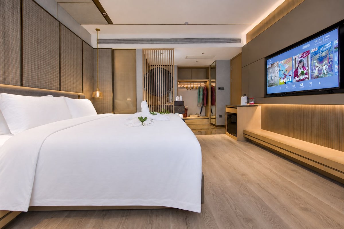 Et moderne hotelværelse med en stor seng, et fjernsyn ophængt på væggen og et walk-in closet.