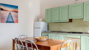 Une cuisine avec des meubles de rangement verts, un réfrigérateur blanc, une table à manger avec des chaises et un saladier rempli de fruits.