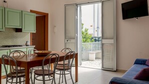 Une cuisine compacte avec un coin repas, un téléviseur fixé au mur et une porte-fenêtre coulissante donnant sur un balcon extérieur.