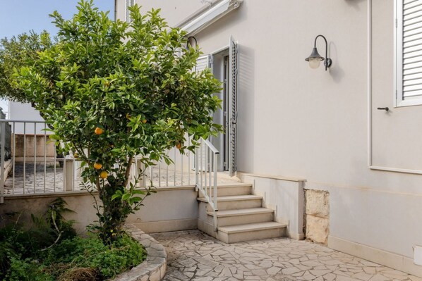A building with a staircase, a tree with fruit, and a wall-mounted light fixture.