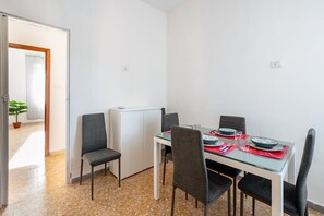 Un coin repas avec une table dressée pour quatre personnes, des chaises, un réfrigérateur et une plante en pot.