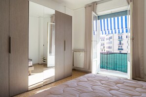Un dormitorio con una cama grande, un armario, un espejo y vistas a edificios a través de una ventana.