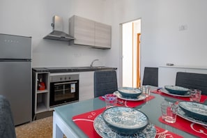 Una cucina moderna con frigorifero, forno e pensili, un tavolo da pranzo apparecchiato con piatti e bicchieri, e vista sull'esterno.