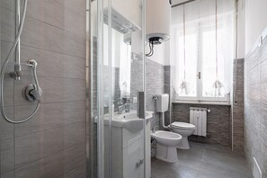 Un baño moderno con cabina de ducha de vidrio, un lavamanos, un inodoro y una ventana con vistas.