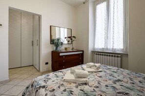 Un dormitorio con cama, cómoda, espejo, ventana con cortinas y radiador.