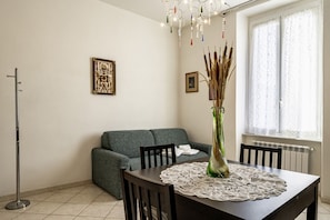 Un comedor con una mesa, sillas, un jarrón con plantas, un sofá y una lámpara de pie.