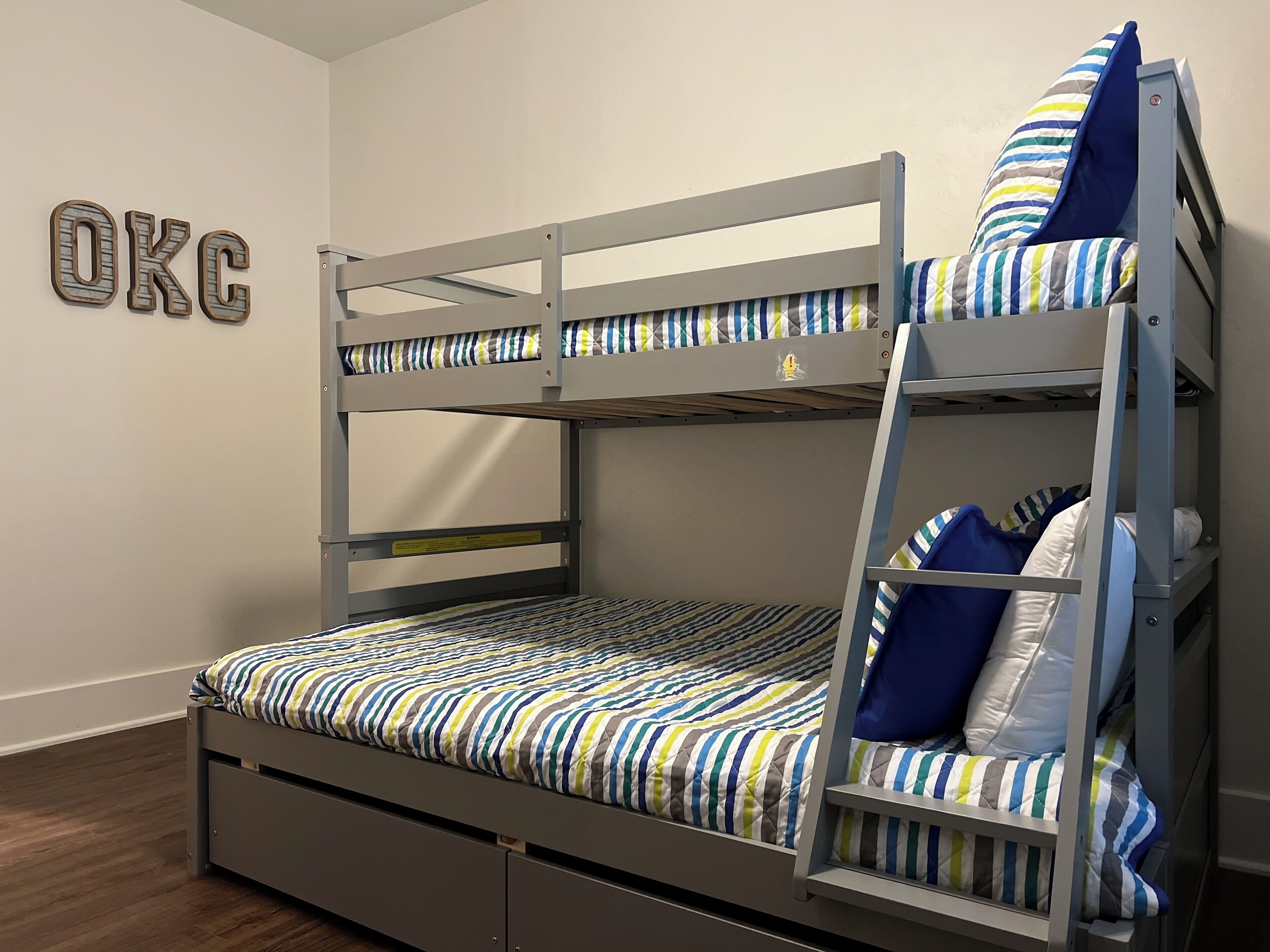 Una cama litera con ropa de cama a rayas, una escalera y un cartel en la pared que dice 'OKC'.