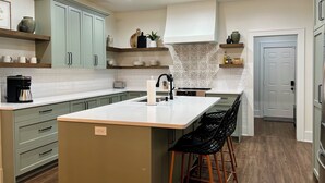 A modern kitchen with light green cabinets, a white countertop, and a central island with bar stools.