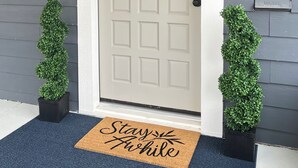A front door with a wreath, a doormat, and two potted plants.