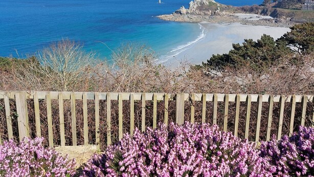 Kustlandschap met een houten hek, strand en rotsformaties.