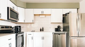 A modern kitchen with white cabinets, stainless steel appliances, and a wooden countertop.