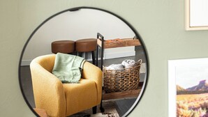 A room with a yellow armchair, a wooden side table, a wicker basket, and a framed picture on the wall.