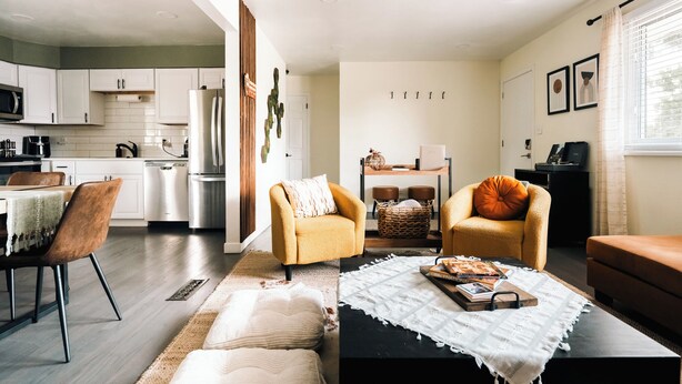A modern living room with a sofa, two armchairs, a coffee table, and a dining area with a table and chairs.