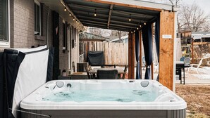 A hot tub in a covered outdoor area with a wooden deck and a table with chairs.