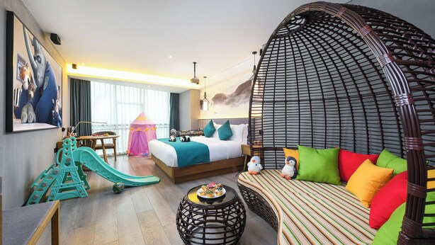 Habitación de hotel con cama, sofá, zona de juegos y un amplio ventanal.