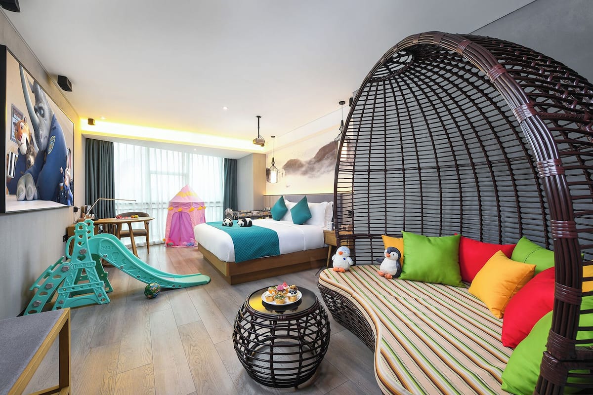 Quarto de hotel com cama, sofá, espaço para brincar e uma janela grande.
