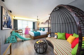 Habitación de hotel con cama, sofá, zona de juegos y un amplio ventanal.