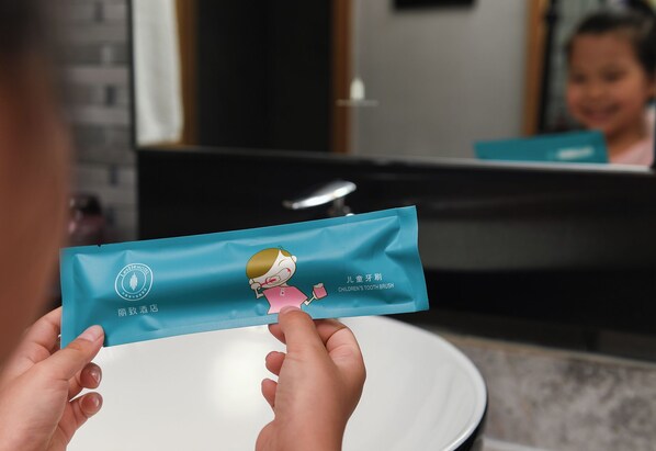 A person holding a children's toothbrush package in front of a bathroom mirror.