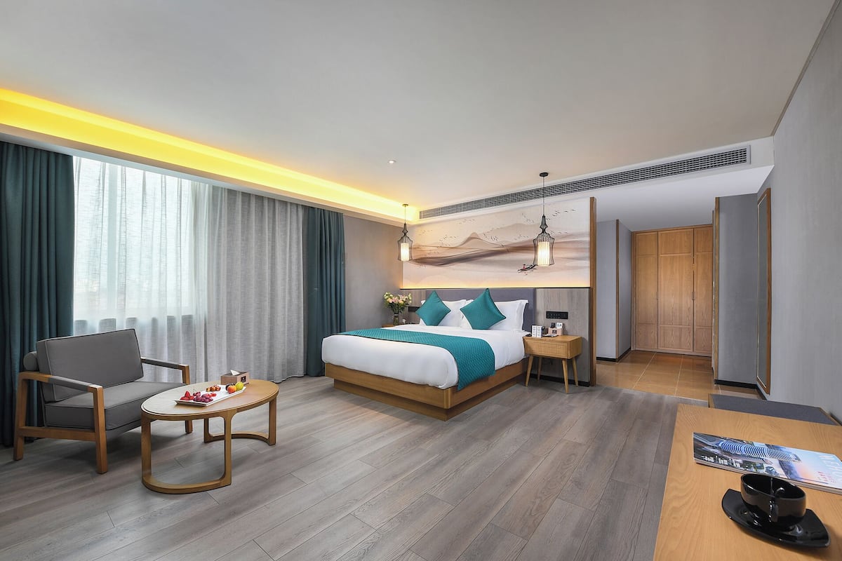 Quarto de hotel moderno com uma cama grande, uma escrivaninha, uma cadeira e uma mesa pequena com fruta.