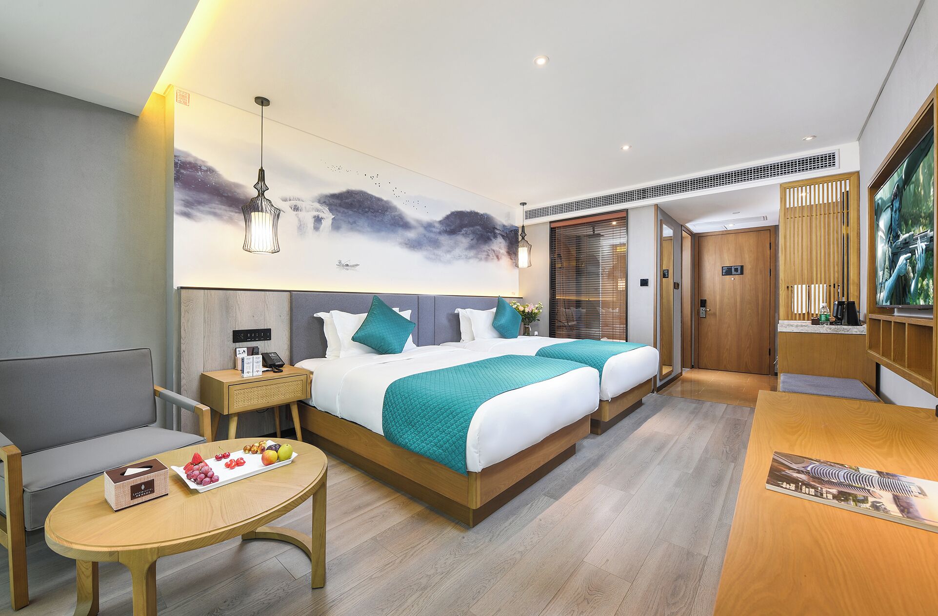 Habitació d'hotel moderna amb dos llits, una escriptori, una cadira, una taula petita amb fruita i un quadre gran a la paret.