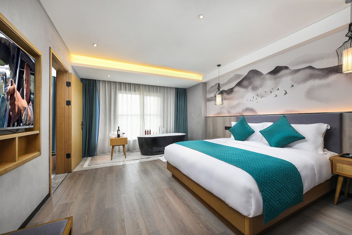 Quarto de hotel moderno com uma cama grande, uma banheira, uma televisão e um mural na parede.