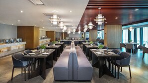 Un comedor moderno con mesas largas, bancos acolchados e iluminación colgante.