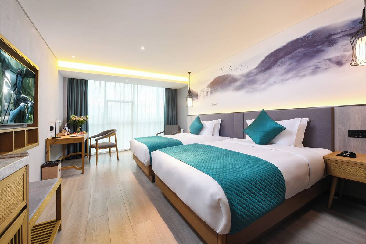 Quarto de hotel com duas camas, uma escrivaninha, uma cadeira e um quadro grande na parede.