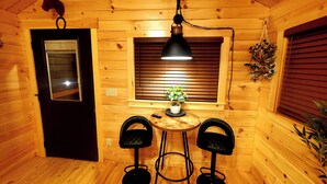 Interior acogedor de una cabaña de madera con una mesa de comedor, dos sillas, una lámpara colgante, una planta en maceta y una decoración con forma de cabeza de caballo.
