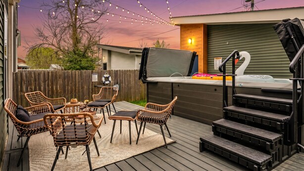 Een terras buiten met rieten meubels, een jacuzzi en lichtjes in de schemering.