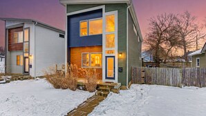 Een modern huis met twee verdiepingen, een duidelijke voordeur, een houten terras en een besneeuwde tuin.