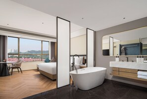 Una habitación de hotel moderna con una cama grande, una zona de estar, una bañera y un baño con tocador y espejo.