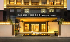 Una entrada de hotel moderna con un estanque reflectante y un letrero que dice 'MEHOOD LESTIE'.
