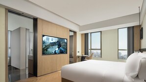 A modern hotel room with a large bed, a TV mounted on the wall, a small table, and a view of the city through large windows. - Mehood Lestie International Hotel Panyu Flagship Branch - Free Shuttle Bus to Canton Fair Complex During Canton Fair Period (Guangzhou)