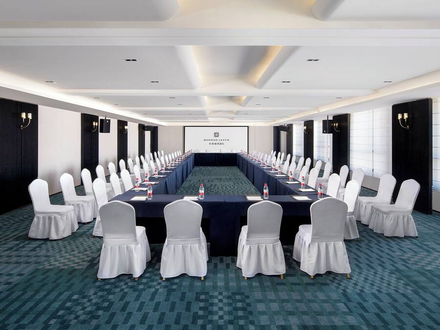Une salle de conférence avec une longue table, des chaises blanches et un écran de projection.
