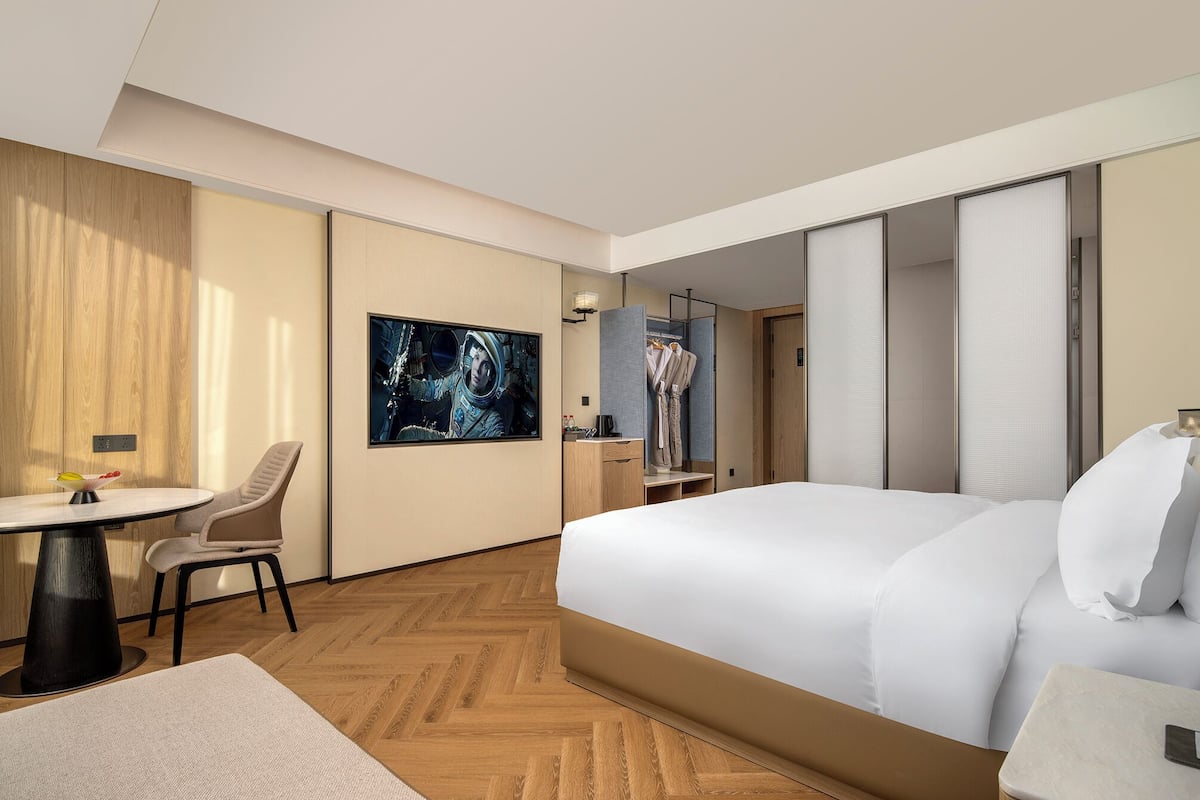 Hotellihuone, jossa on suuri sänky, työpöytä tuolilla, pieni pöytä ja taulu seinällä.