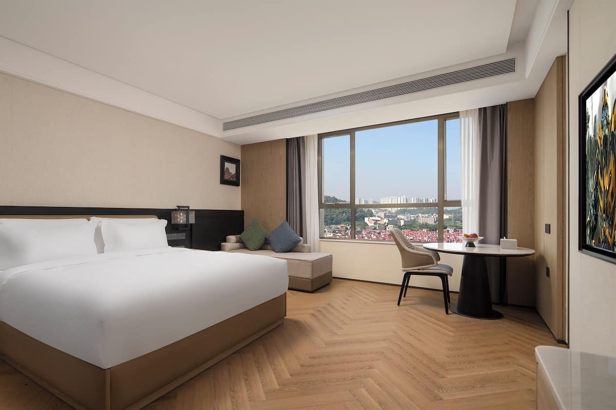 Moderni hotellihuone, jossa on suuri sänky, työpöytä ja näkymä kaupunkiin.