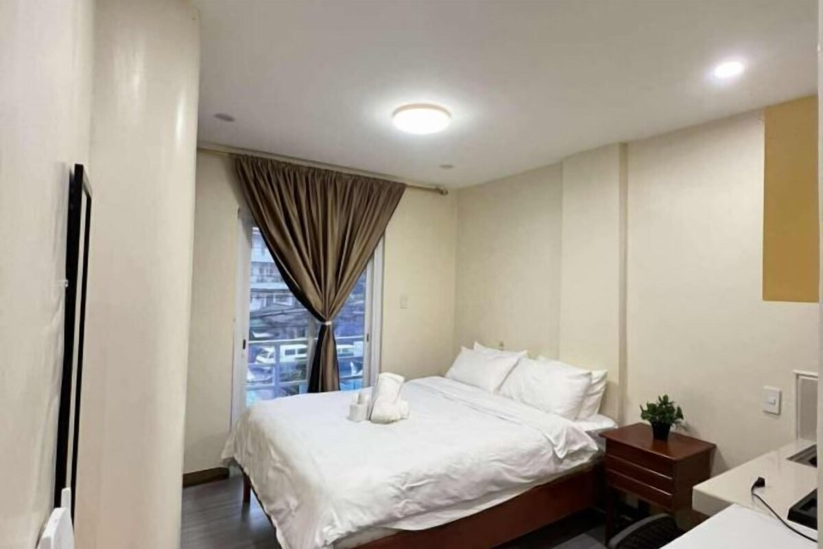 Ein Hotelzimmer mit Bett, Schreibtisch, Sessel, Pflanze und einem fensterbepflanzten Fenster.
