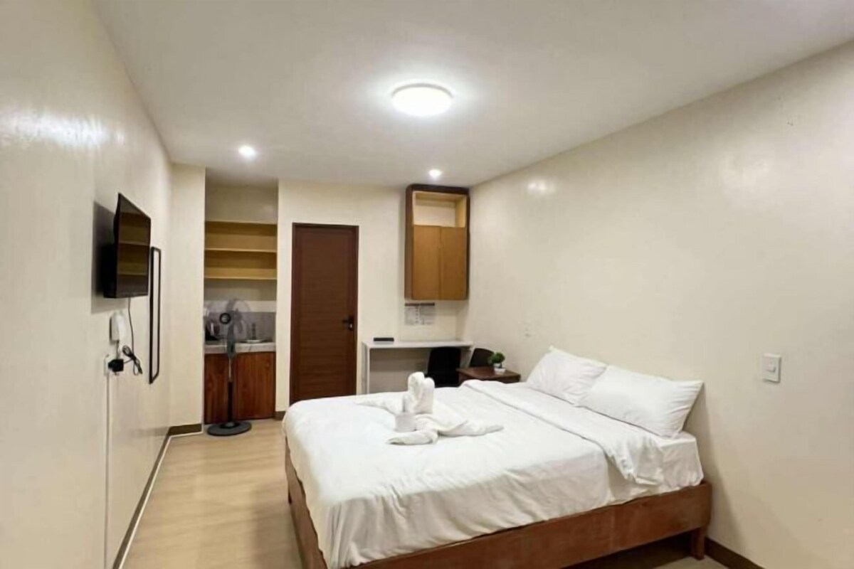 Ein Hotelzimmer mit einem Bett, einem an der Wand montierten Fernseher, einer Holztür und einem kleinen Tisch mit einer Pflanze.