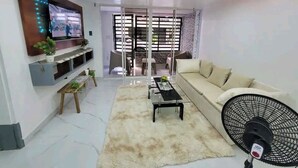 A modern living room with a sofa, a coffee table, a TV mounted on the wall, and a fan. - Obynb premium  (Santo Domingo)
