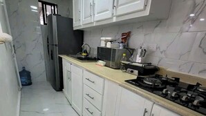 A modern kitchen with white cabinets, a stainless steel refrigerator, a gas stove, and a microwave. - Obynb premium  (Santo Domingo)