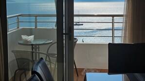 Un balcón con vistas al mar y a las montañas, una mesa con un cuenco decorativo y una silla.