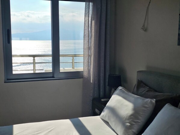 Une chambre d’hôtel avec un lit, une table de chevet, une lampe et une fenêtre donnant sur la mer et un pont.
